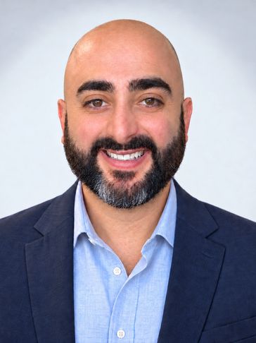 Smiling bald man with a beard in a suit jacket and light blue shirt.