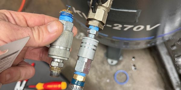 Hand holding air compressor fittings with 270V tank in background.