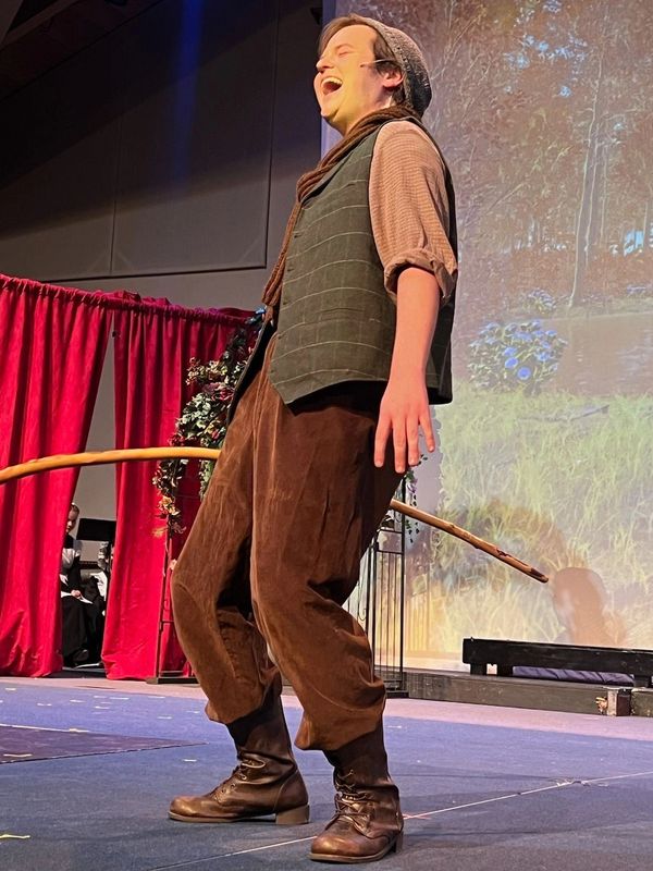 David is standing on a stage singing the role of Dickon in The Secret Garden. To his right is a red 