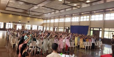 A large group of people raising hands in a spacious hall during an event.