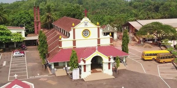 A church with a red roof surrounded by trees and parked vehicles.