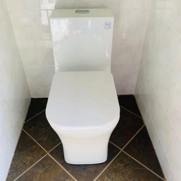 A modern white toilet installed between tiled walls.