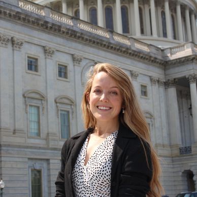 Smiling woman standing in front of a historic government building.