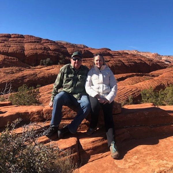 A couple sits on red rock formations under a clear blue sky.