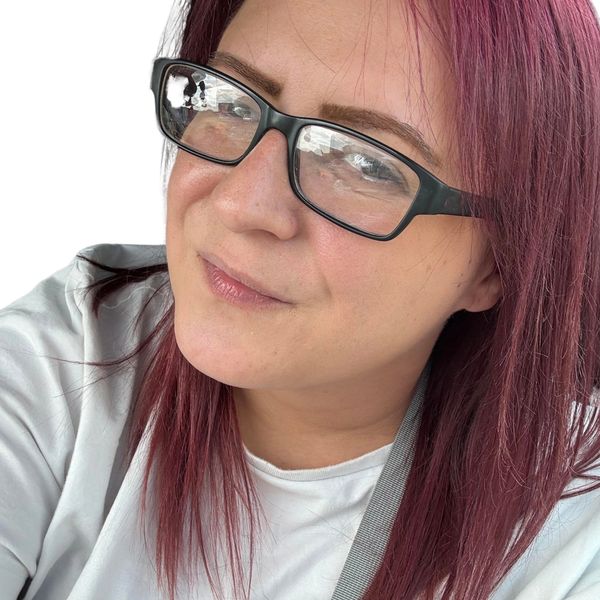 Woman with purple hair and glasses smiling gently.
