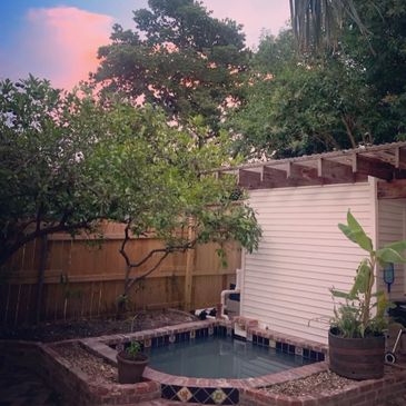 Cozy backyard with small pool, greenery, and pink sunset sky.