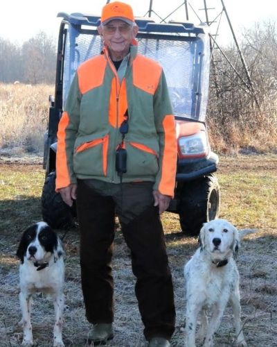 Older man in hunting gear with two dogs.