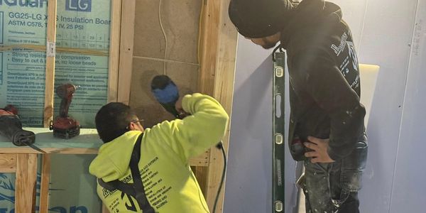 Two workers installing insulation and drywall in a construction area.