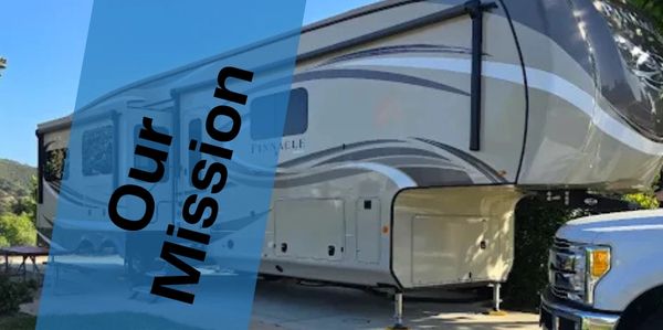 A large RV trailer parked with a truck nearby under clear blue sky.