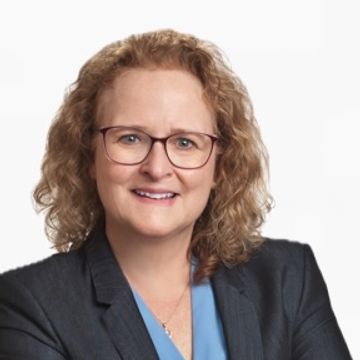 Professional woman with curly hair wearing glasses and a blazer.