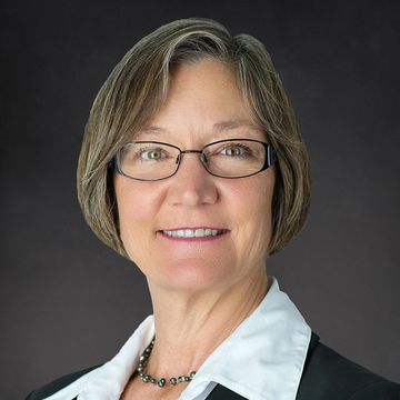 Smiling woman with short hair and glasses in a black blazer.