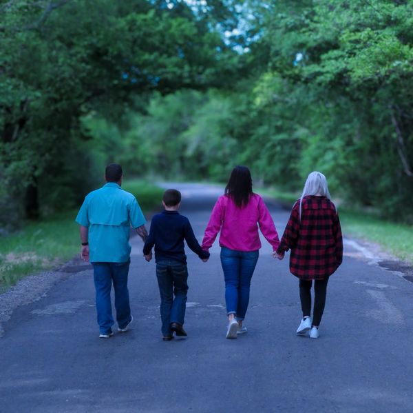 A family of four holding hands walking down a tree-lined road.