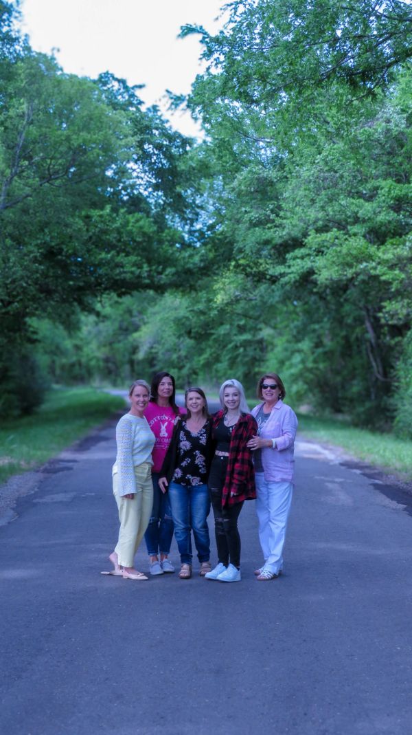Five women stand together on a forest path, smiling for a group photo.