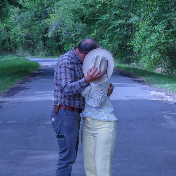 Couple sharing a kiss behind a hat on a quiet forest road.