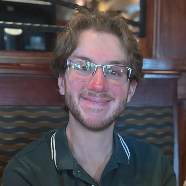 Young man with glasses smiling indoors at a restaurant.