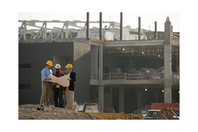 Three construction workers discuss plans at a building site wearing safety helmets.