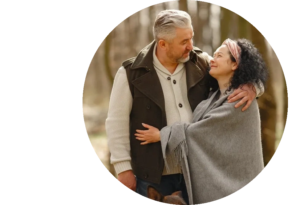 Middle aged couple hugging in the woods looking at each other lovingly. 