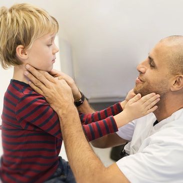Doctor gently examines young boy's throat during checkup.