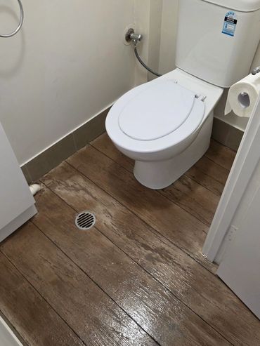 Tiled flooring in a toilet, resurfaced with Concrete Timber Look  Overlay  by Spray Pave Wide Bay.