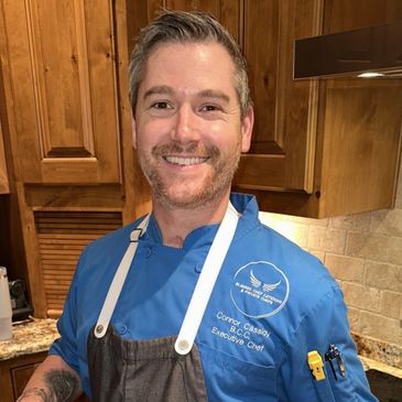 Smiling chef in blue uniform standing in a kitchen.