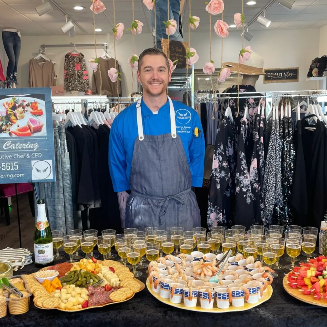 Chef standing behind a table with food and drinks in a clothing store.