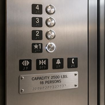 Elevator control panel with buttons and capacity sign inside a stainless steel elevator.
