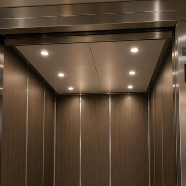 Interior of a modern elevator with wooden panels and recessed ceiling lights.