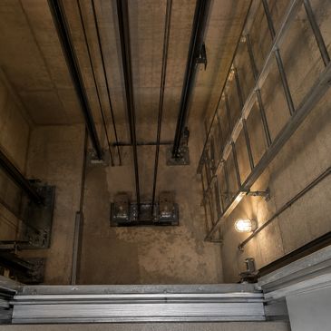 View down an empty elevator shaft with cables and lighting.