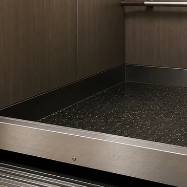 Close-up of an elevator floor and interior corner with wood paneling and metal trim.