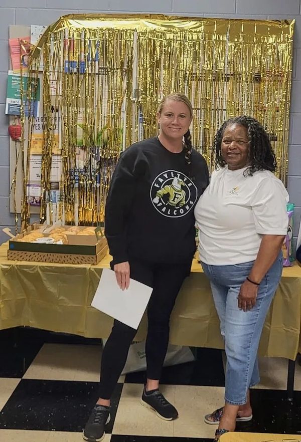 Two women posing in front of a gold-decorated table with snacks.
