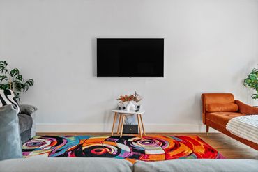 A painted white living room featuring stylish orange, grey, and white furniture and TV