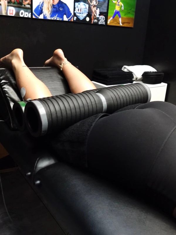 Person lying on table with black cylindrical device on legs.