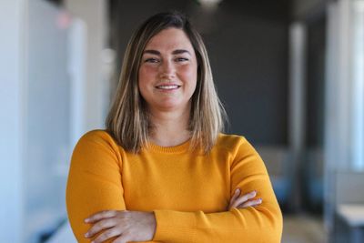 Confident woman in a mustard yellow sweater smiling with arms crossed.