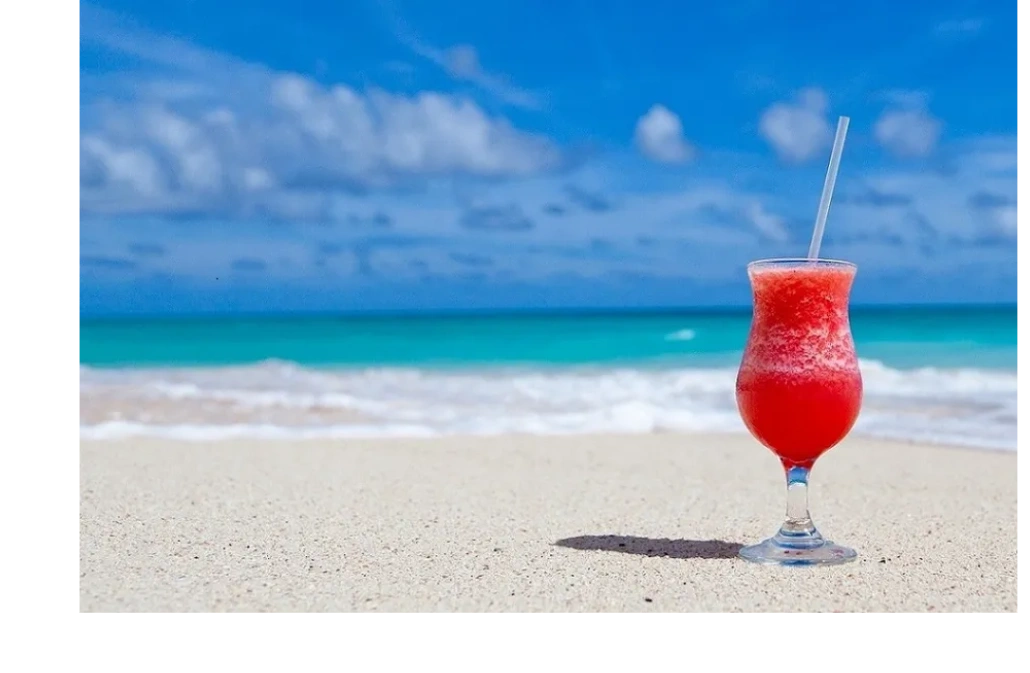 A bright sunny day on a private beach with teal calm water and a delicious red frozen drink