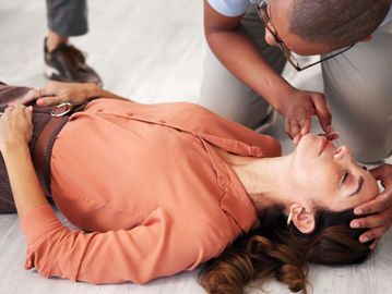 Person performing CPR on a woman lying on the floor.