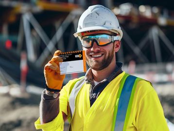 Construction worker smiling, holding an ID card at a site.