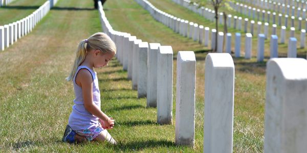 A young girl kneeling in a cemetery among rows of white gravestones.