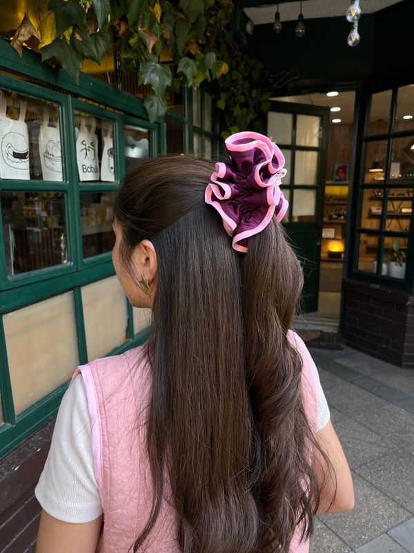 Mujer con cabello largo y coleta rizada con moño rosa.