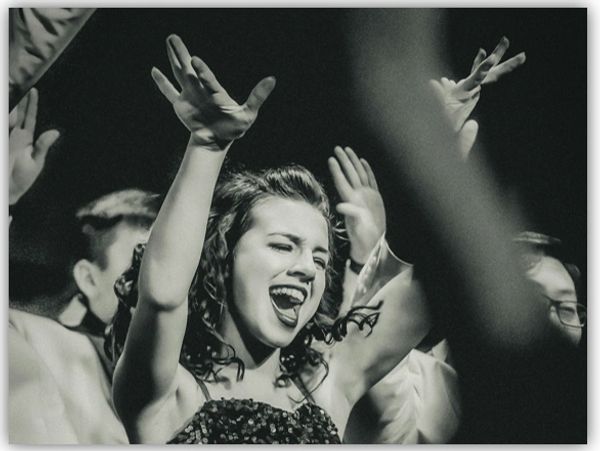 woman with hands raised, singing passionately