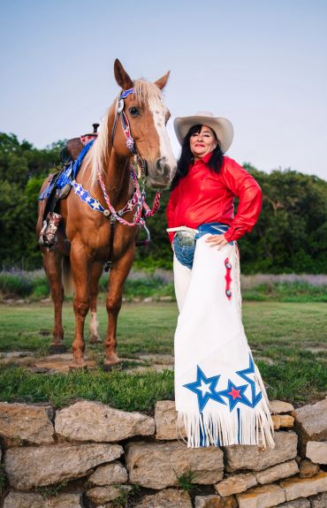 A woman in western attire poses with a decorated horse outdoors.