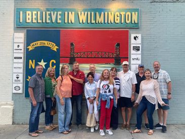 Group poses in front of Wilmington mural with NC flag.
