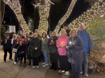 Group of people posing outdoors at night with trees wrapped in lights.