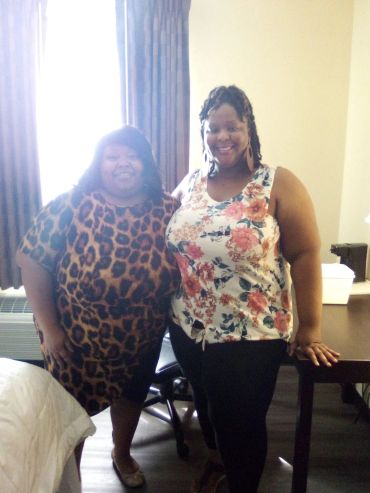 Two women smiling indoors, one in a leopard print dress and the other in a floral top.