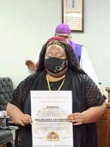 Woman holding a certificate wearing a mask, man standing behind.