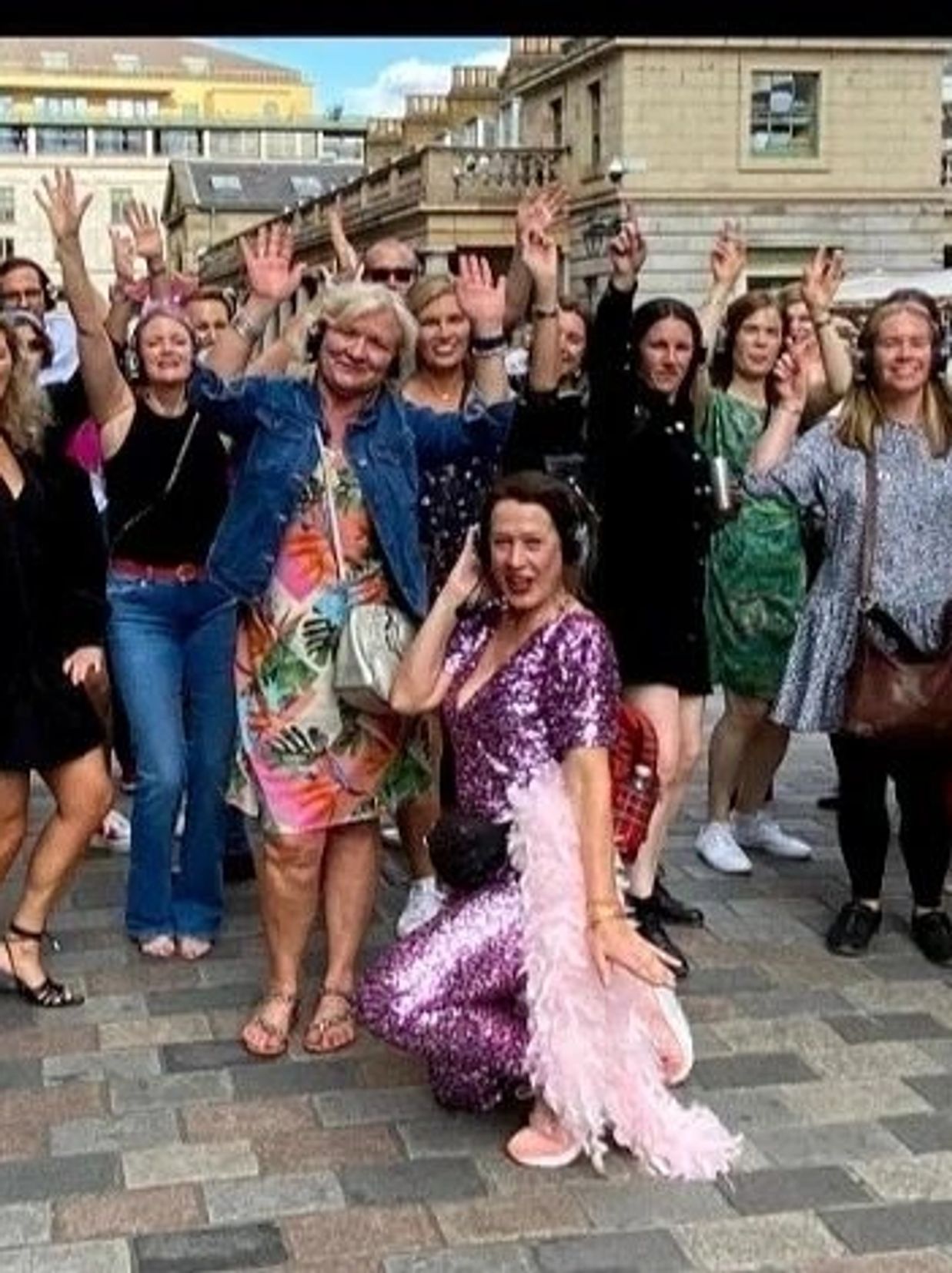 Group of people joyfully raising hands outdoors in a lively urban setting.