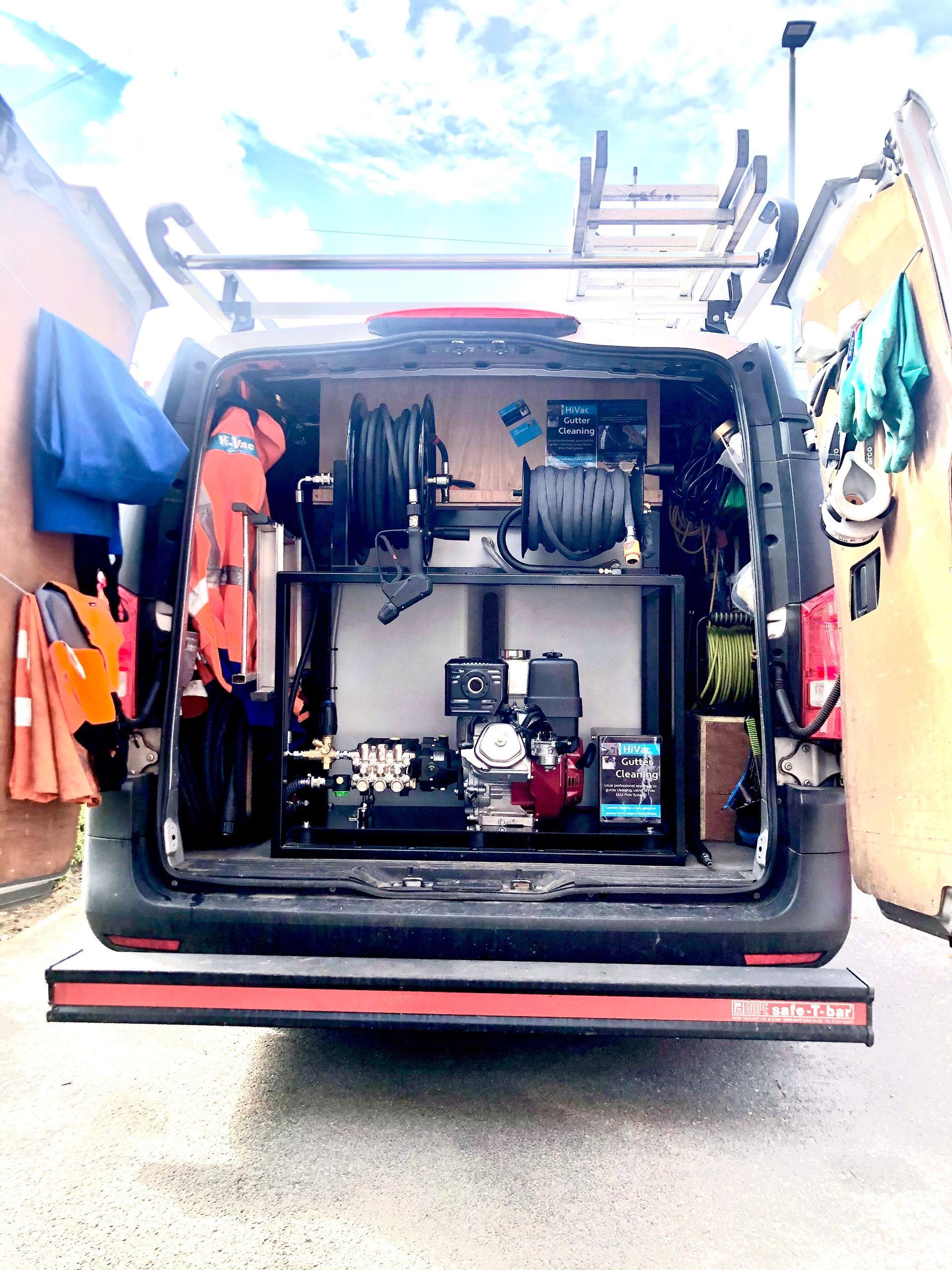 Open van equipped for gutter cleaning with hoses and safety gear.