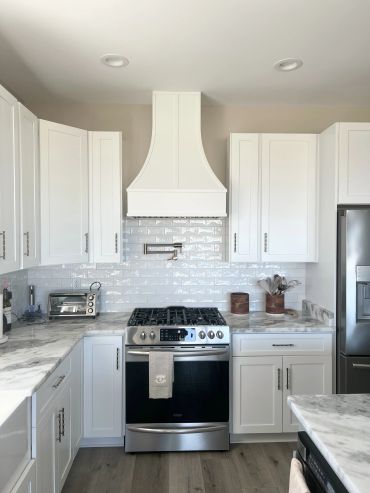 Modern kitchen with white cabinets, marble countertops, and stainless steel appliances.