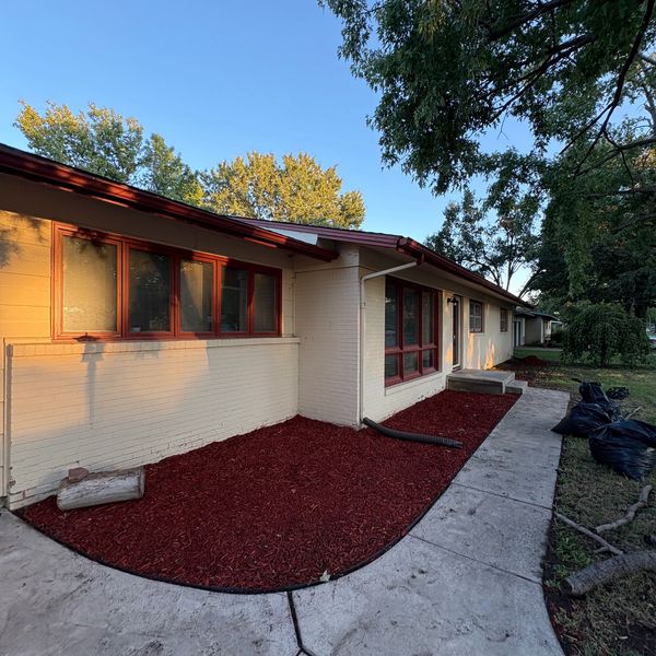 Freshly mulched front yard of a single-story house with beige walls and red window frames.