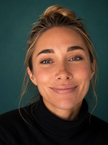 Close-up portrait of a smiling woman with a bun and black turtleneck.
