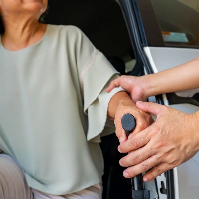 Helping elderly person with cane get into car.